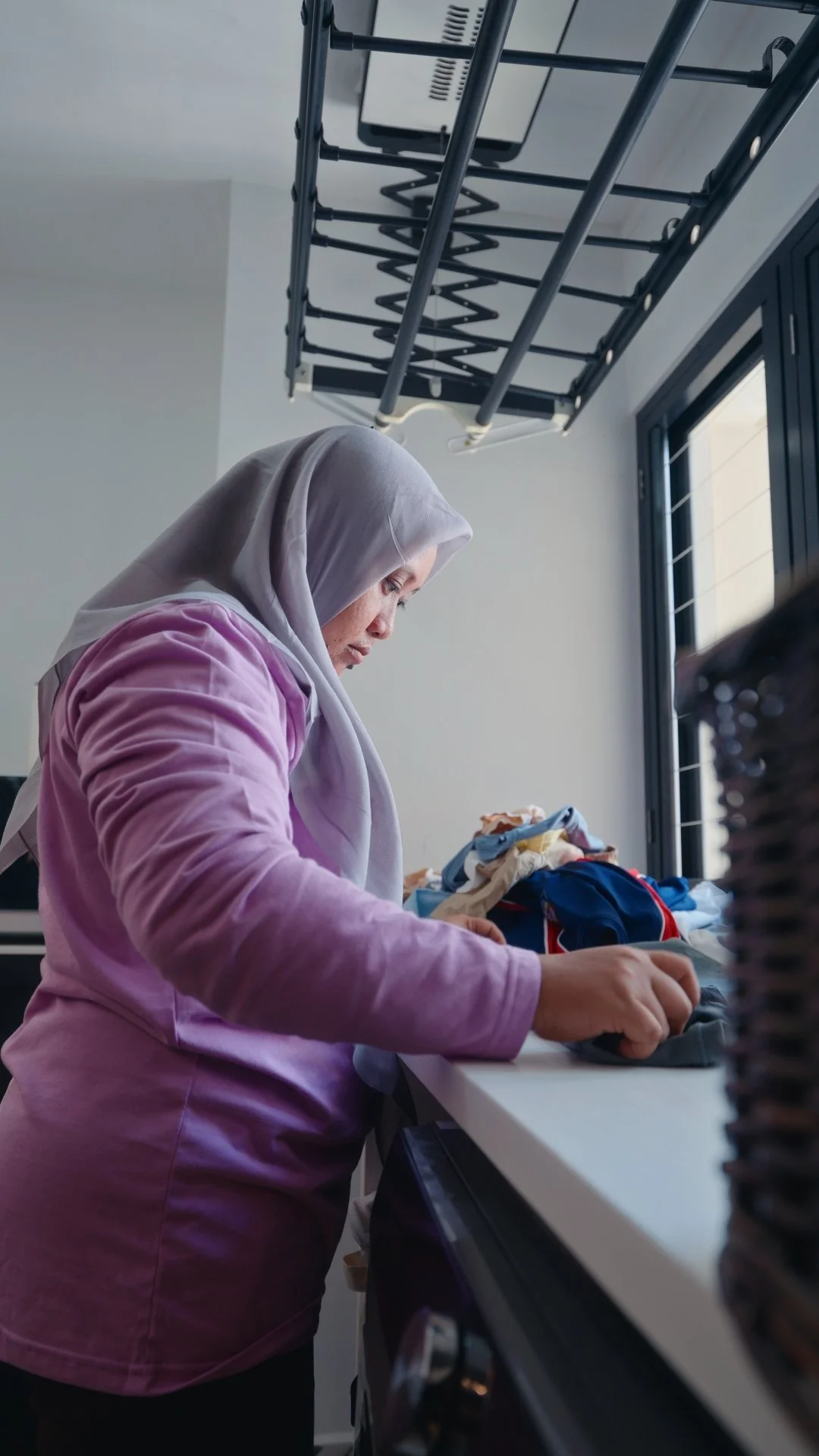A domestic helper sorting and folding laundry at a table in a Singapore home