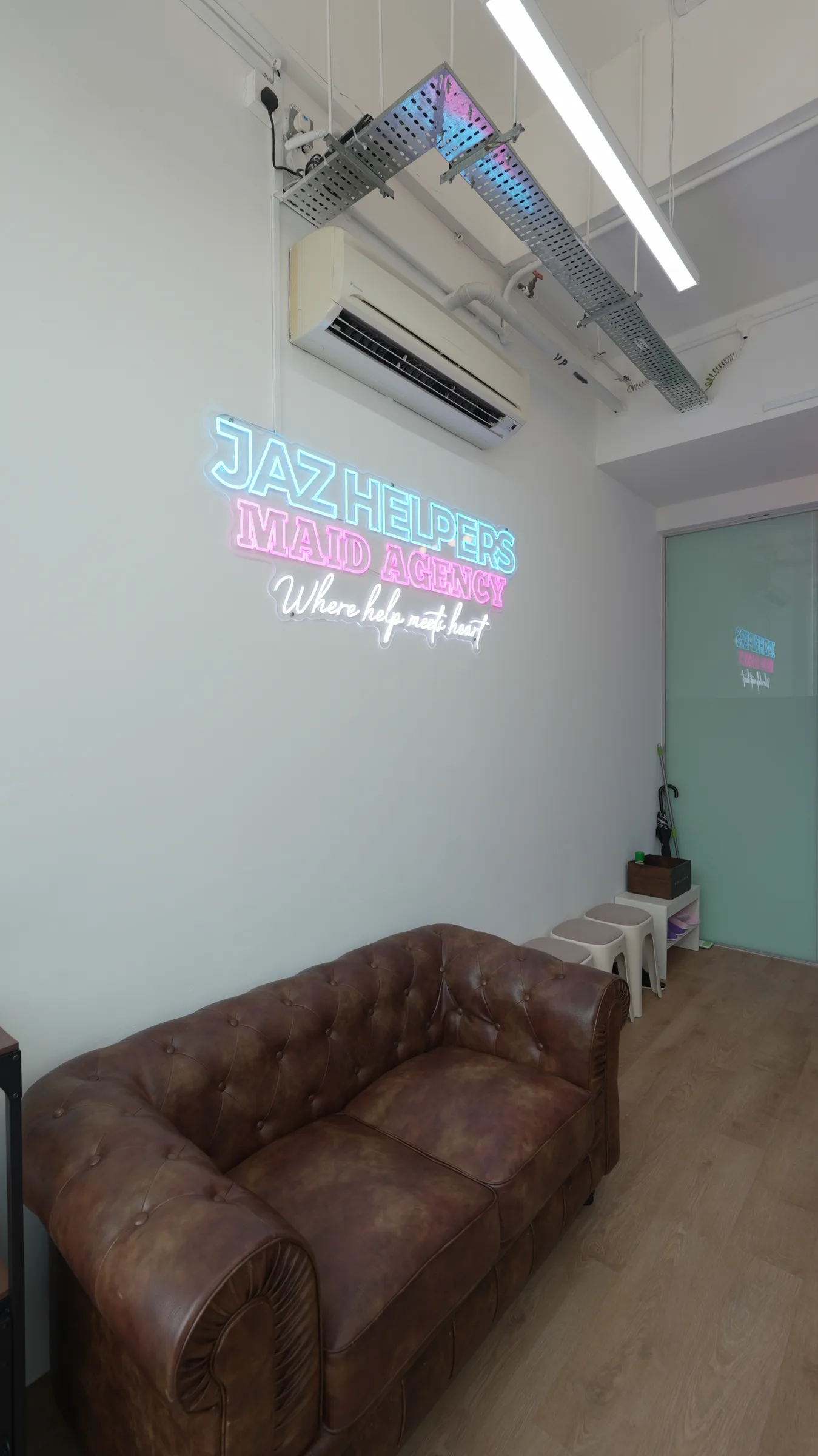The Jaz Helpers waiting area: a leather sofa beneath the Jaz Helpers Maid Agency neon sign